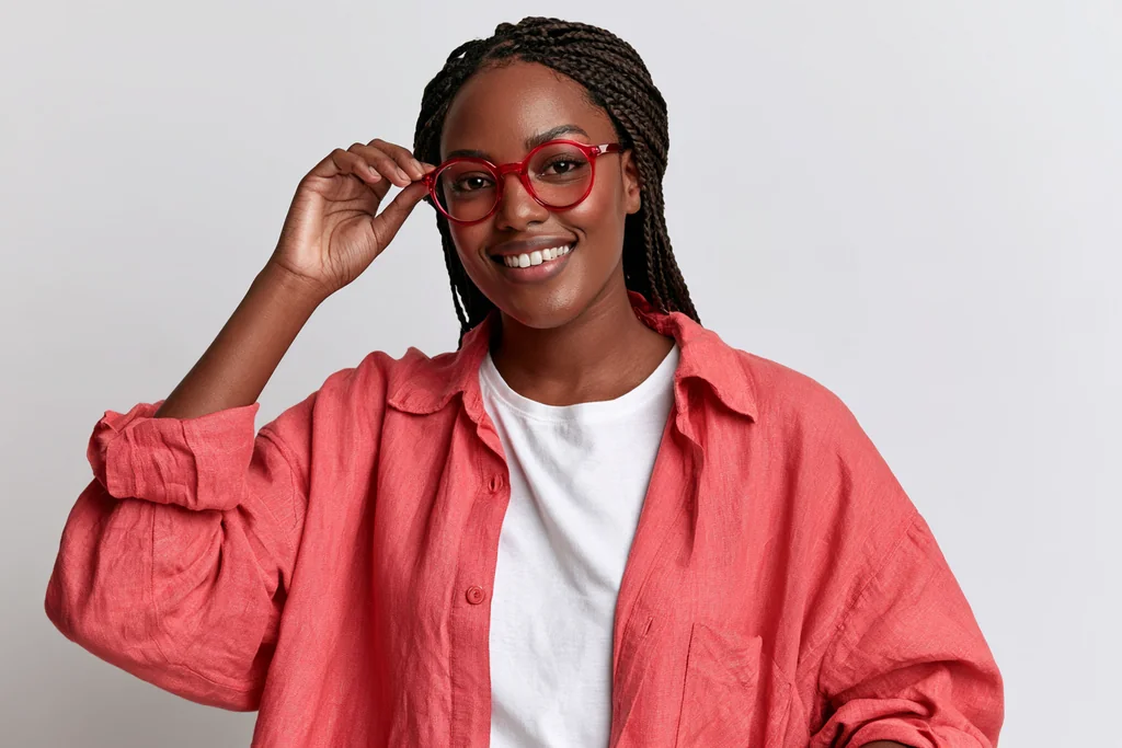 Young woman with braids in red glasses and an open coral linen shirt, light gray studio
