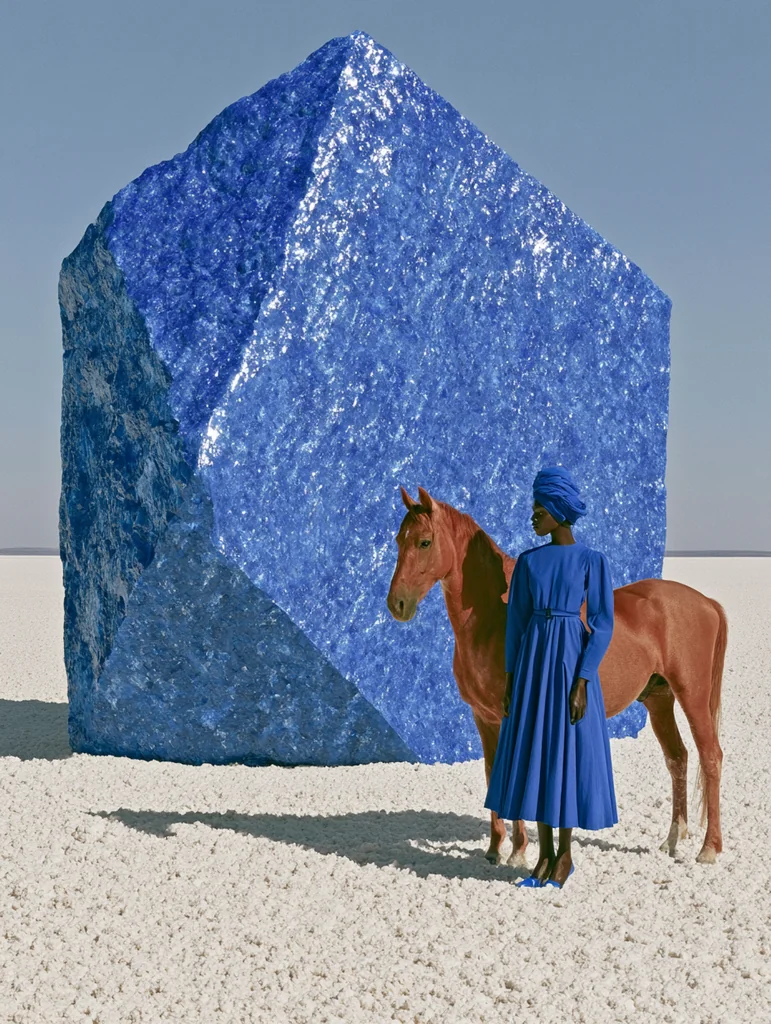 A woman in a cobalt dress beside a reddish horse and a giant cobalt mineral form on a white salt flat