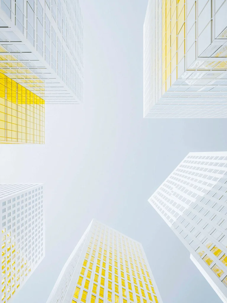 White towers with lemon yellow glass seen from below, converging around a pale gray sky