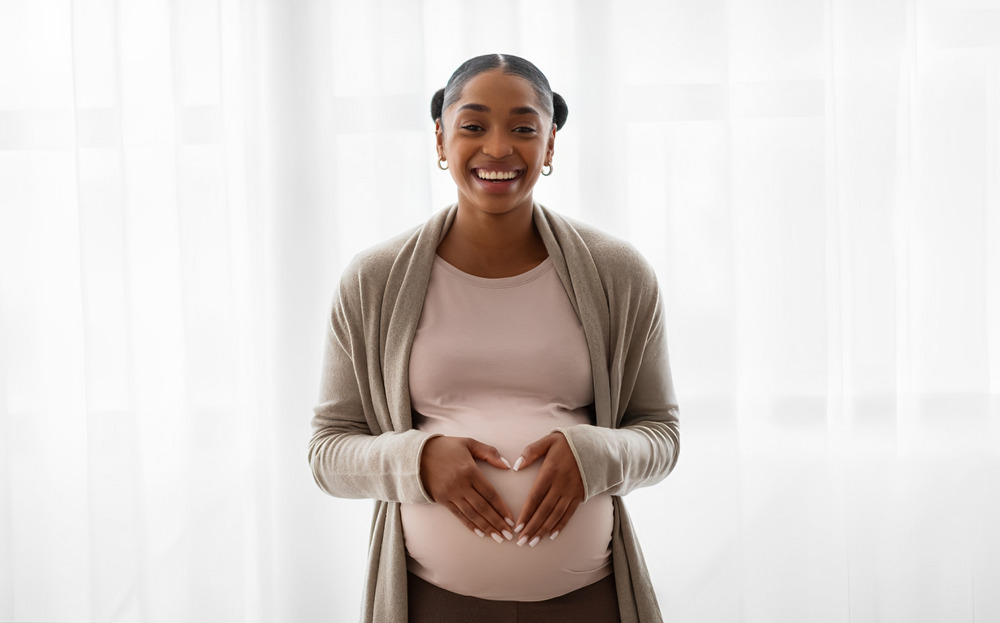 Happy pregnant woman holding palms in heart shape on tummy stock photo