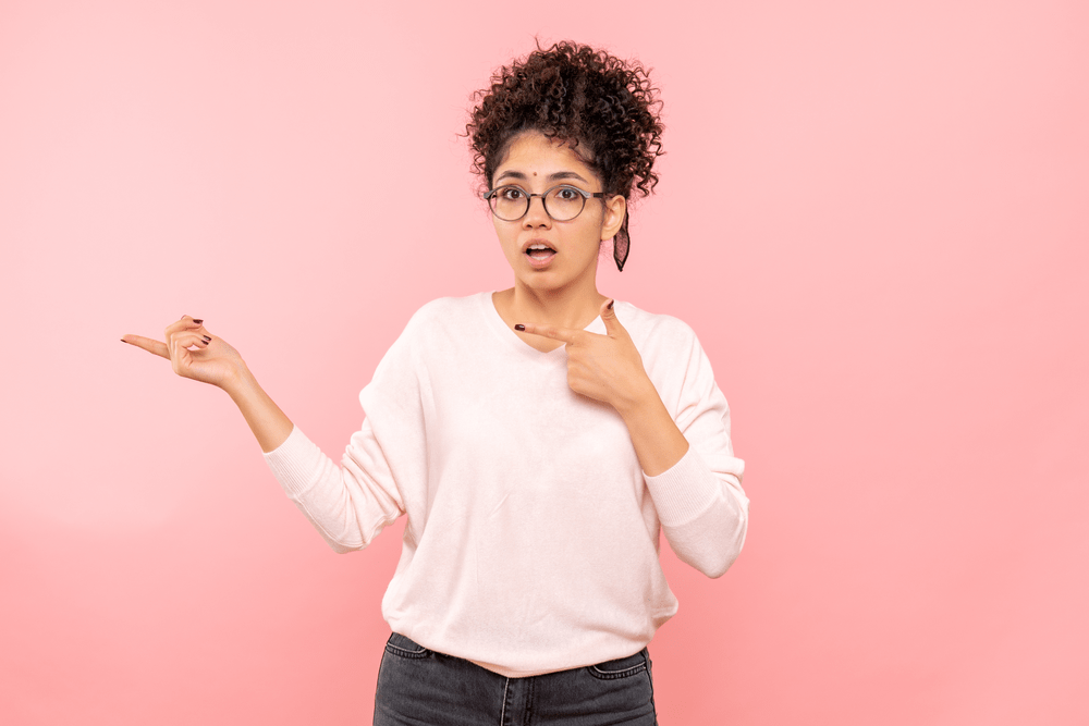 Surprised Young Woman Pointing on Pink Background