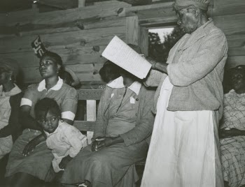1939 - Star pupil, 82 years old, reading her lesson in adult class, Gee's Bend, Alabama.