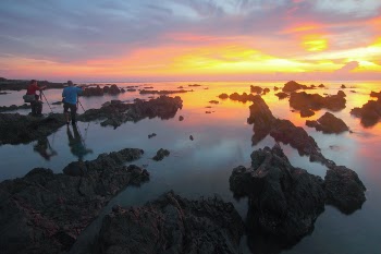 2 People Standing on Rock Formation Reflected on Water during Sunset