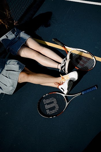 2 Women Sitting on Tennis Court Besides 2 Wilson Tennis Rackets