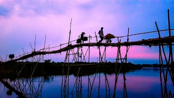 3 Person Walking on Bridge Under Cloudy Sky during Sunrise