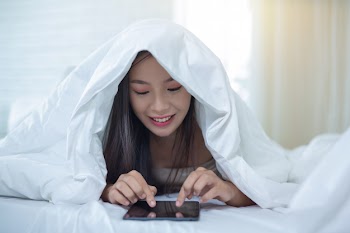 A beautiful asian woman relaxes and works with a laptop computer, reading at home. Free Photo