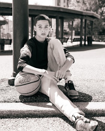 A Boy Sitting Besides The Post Of A Basketball Hoop