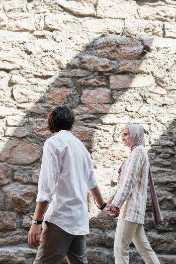A Couple Holding Each Others Hand while Walking Near the Stone Wall · Free Stock Photo