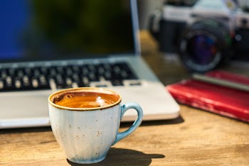 A cup of coffee and a camera on a wooden table  in the workplace  