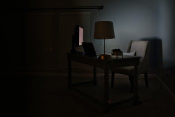 A desk with computers on it taken at night in a dark room.
