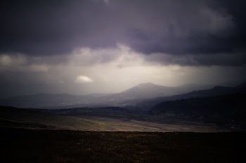 A dim shot of plains stretching to the low mountains on the horizon under gray clouds