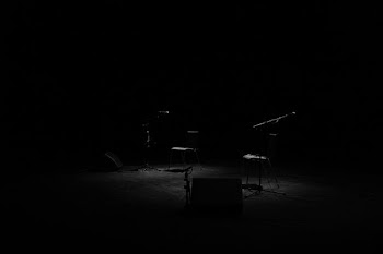 A dim shot of two chairs and microphone stands on an empty stage