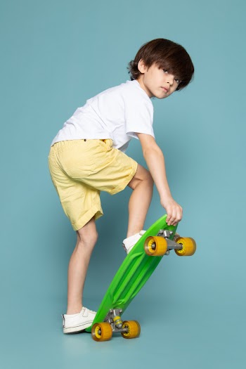 A front view child boy in white t-shirt and yellow jeans riding green skateboard on the blue space Free Photo