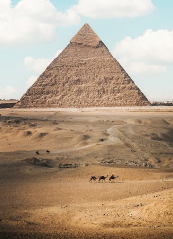 a group of people riding camels in front of a pyramid