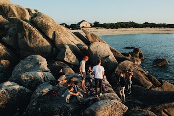 A Group Of Young People Lazing Around The Boulders By The Sea Close To The Shoreline