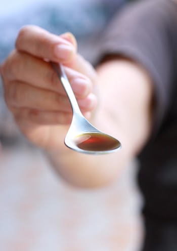 a hand holding a teaspoon of liquid medicine