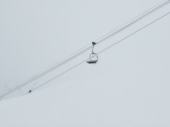 A lone ski lift chair traveling down the mountain against an empty sky.