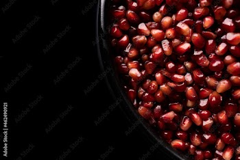 A lot of beautiful red pomegranate seeds in a black bowl