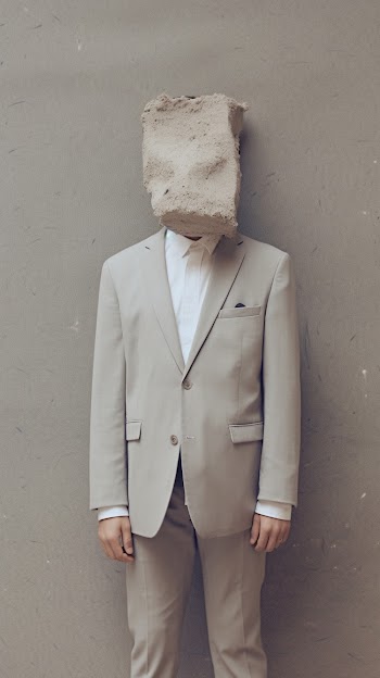 A man in a light grey suit with his face covered by a cement block