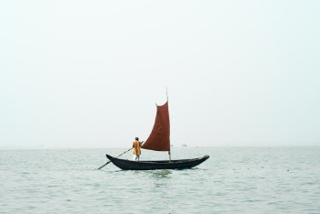 A Man Rowing A Small Boat With a Sail