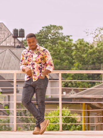 A man wearing a floral shirt and jeans leaning on a fence
