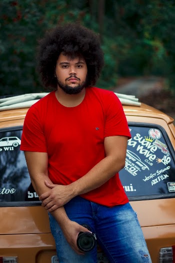 A man wearing a red t shirt leaning on a car
