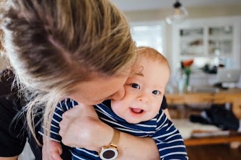 A mom kissing her smiling baby on the cheek.