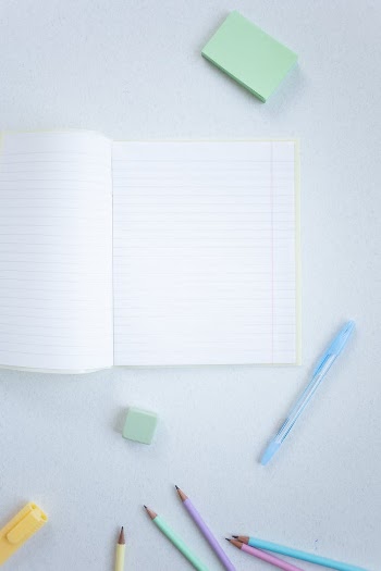 A Notebook and Coloring Materials on a White Surface