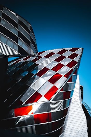 A partial exterior of a modern curvy architectural building, with red and clear glass panes