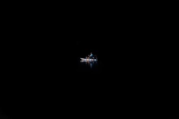 A person on a canoe in the water surrounded by complete darkness.