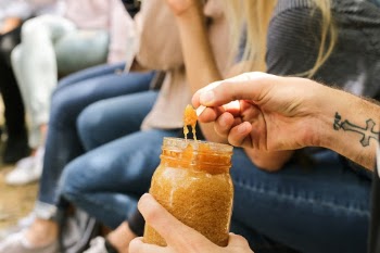 A person with a tattoo trying a sample of natural homemade honey