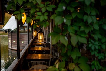 A Row Of Brown Wooden Tables With Pendant Lights In An Establishment By A Calm Body of Water