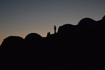 A silhouette of a person in a camping site on a slope at night