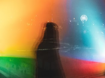 A snapshot of the reflection of two colour lamps in the Kiasma museum of modern art in Helsinki. A woman happened to pass by when I was looking to the window.