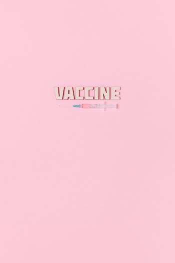 A Syringe and Vaccine Text on Pink Background