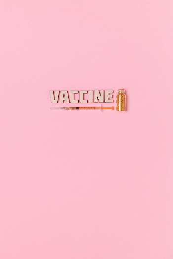 A Syringe and Vaccine Text on Pink Background