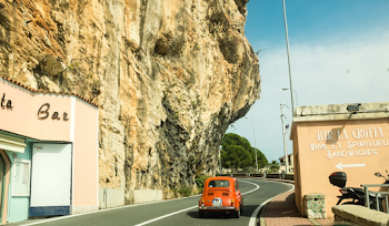 A Vintage Red Car Driving Down A Windy Road On The Side Of A Cliff ...
