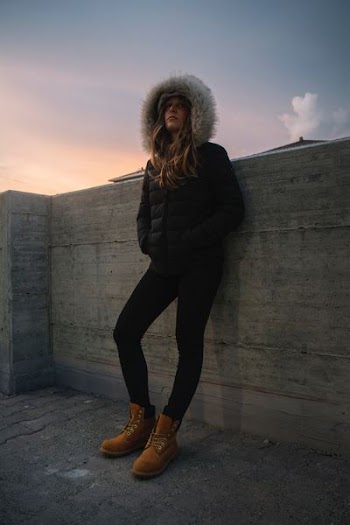 A woman in a parka and Timberland boots leans against a wall