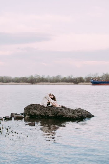 A Woman in White Long Sleeves Sitting on the Rock Near Body of Water · Free Stock Photo