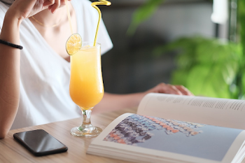 A Woman Reading And Drinking Juice On Table With An IPhone On It ...