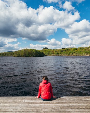 A woman sitting on the shore of a large lake.