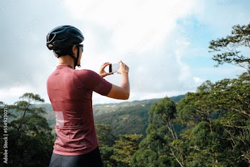 A young female cyclist is taking photos with her mobile device in the mountains.