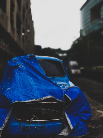 Abandoned Classic Blue Car With Blue Tarp Parked Beside Concrete Building