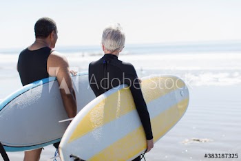 Active senior couple carrying surfboards on sunny beach