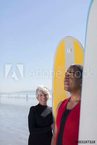 Active senior couple with surfboards on sunny beach