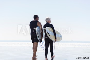 Active senior couple with surfboards on sunny beach