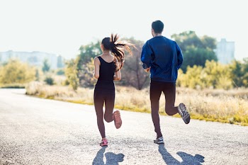 Active sporty woman and man jogging on sunny day in park. Couple in tracksuits running along the road. Healthy lifestyle, sport, healthcare concept. Full-length portrait of two people, back view
