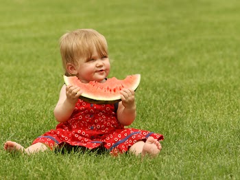 adorable little baby sitting on the grass with a piece of watermelon