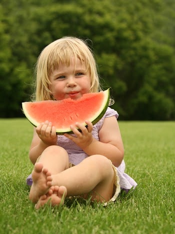 adorable little toddler sitting on the grass with a piece of watermelon