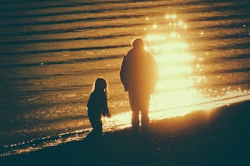 adult and child near seashore during sunset